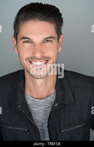 Un beau homme souriant, un homme caucasien posant une tête de vue souriant devant un fond gris. Un portrait de studio. Banque D'Images