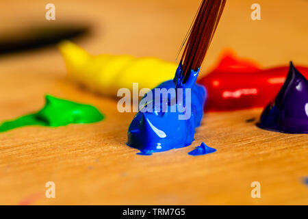 Forte d'une macro d'artiste d'être chargé de la peinture acrylique bleu à partir de taches de peinture sur une palette d'une roue de couleurs primaires et secondaires. Banque D'Images