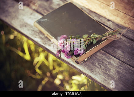 Fleurs de trèfle rose fluffy sont réunis dans un bouquet et attaché avec la corde de chanvre. Ils se trouvent avec livre fermé sur une table en bois. Banque D'Images