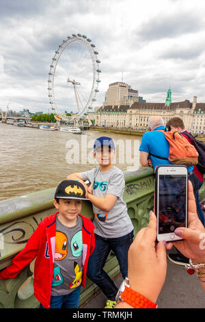 Une mère prend une photo de ses jeunes enfants de Westminster Bridge avec le London Eye en arrière-plan sur une excursion d'une journée à Londres Banque D'Images