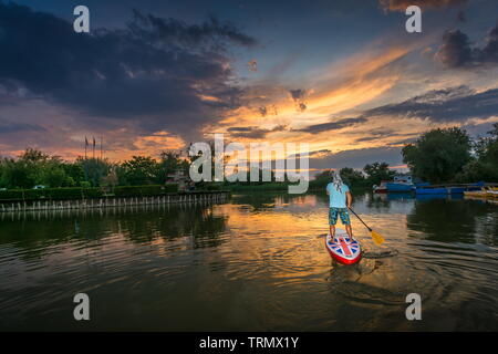 Gura Portitei, Roumanie - 08 juin 2019 : l'homme sur le SUP, Stand up Paddling au coucher du soleil sur le lac dans le Delta du Danube à Gura Portitei, Roumanie Banque D'Images