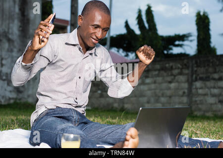 Businessman sitting in garden à joyeusement à son ordinateur portable Banque D'Images