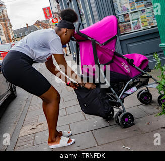 Une jeune mère de minorités ethniques à participer à sa fille qui est in a purple Mamas and Papas poussette de bébé Banque D'Images