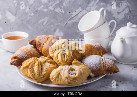 Pâte feuilletée sucré et frais couverts avec du sucre en poudre sur une table gris à côté de la bouilloire et tasses pour le thé Banque D'Images