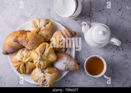 Pâte feuilletée sucré et frais couverts avec du sucre en poudre sur une table gris à côté de la bouilloire et tasses pour le thé Banque D'Images