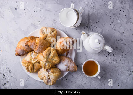 Pâte feuilletée sucré et frais couverts avec du sucre en poudre sur une table gris à côté de la bouilloire et tasses pour le thé Banque D'Images