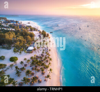 Vue aérienne de parasols, palmiers sur la plage de sable de la mer au coucher du soleil. Voyage d'été à Zanzibar, Afrique. Paysage tropical avec palmiers, bateaux, Banque D'Images
