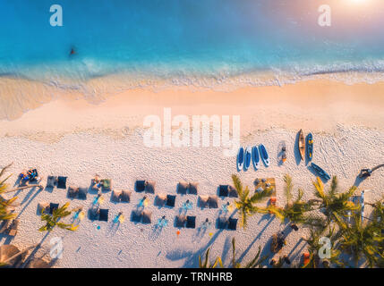 Vue aérienne de parasols, palmiers sur la plage de sable de la mer bleue au coucher du soleil. Voyage d'été à Zanzibar, Afrique. Paysage tropical avec des palmiers, par Banque D'Images