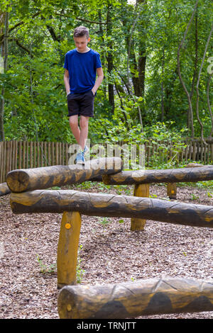 Les jeunes 11 ans caucasien garçon extérieur en été à l'équilibre sur le serpent en bois au jeu naturel d'une aire de jeux construits de bois sculpté Banque D'Images