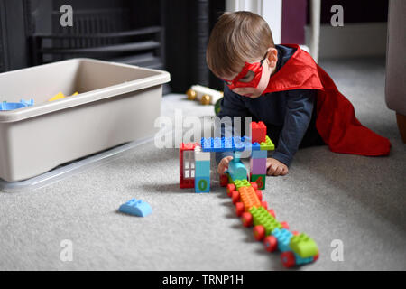 Un garçon en robe d'un capuchon et le masque joue avec des blocs Lego Duplo Banque D'Images