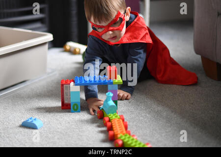 Un garçon en robe d'un capuchon et le masque joue avec des blocs Lego Duplo Banque D'Images