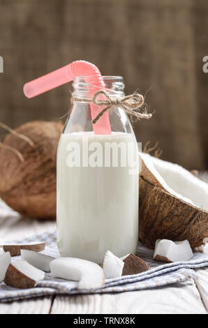 Le flacon en verre de lait ou de yogourt sur bleu serviette sur une table en bois blanc à la noix de coco de côté Banque D'Images