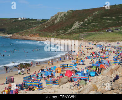 Une foule de gens qui profitent d'une journée d'été ensoleillée sur la plage de Sennen Cove Cornwall, Angleterre, Royaume-Uni, montrant la plage de sable et la mer bleue sous un ciel bleu. Banque D'Images