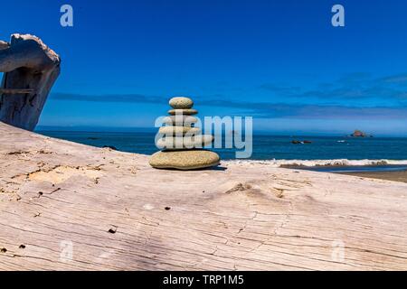 Cairn de pierres équilibré sur une bûche de bois flotté à Ruby Beach avec des piles de rochers en arrière-plan, Parc national Olympique, Washington, États-Unis Banque D'Images