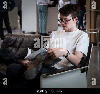 Une ambiance jeune homme de race blanche sur un canapé Vitsœ la lecture d'un magazine. Banque D'Images