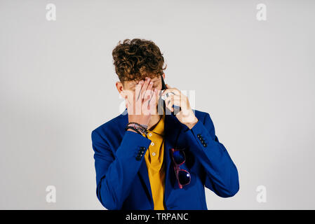 Young caucasian homme habillé avec un costume bleu de parler par téléphone et met la main sur son visage Banque D'Images