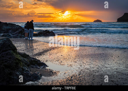 Deux jeunes hommes sur la rive à regarder la marée montante au coucher du soleil. Polzeath, Cornwall, England UK Banque D'Images