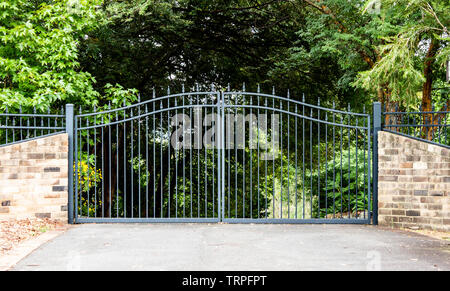 L'entrée des portes d'entrée métalliques propriété situé dans le jardin avec clôture en brique d'arbres en arrière-plan Banque D'Images