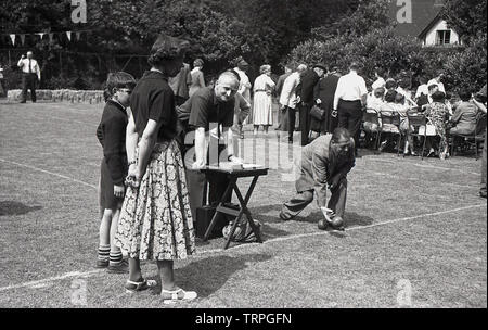 1955, historique, un jeu de boules sur gazon ou à d'une fête du village, un homme portant un costume en laine en se penchant pour jeter un bol sur l'herbe, suivi par sa femme et son fils, England, UK. Banque D'Images