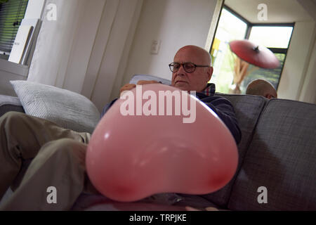 Personnes âgées retired man sauter un gros ballon rose en forme de coeur pour décorer la salle pour un anniversaire Banque D'Images