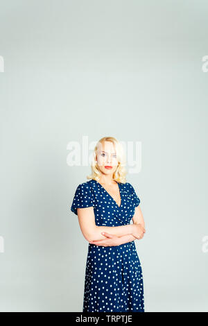 Portrait de studio de belle blonde femme dans une robe bleu foncé blanc contre fond uni Banque D'Images