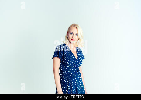 Portrait de studio de belle blonde femme dans une robe bleu foncé blanc contre fond uni Banque D'Images