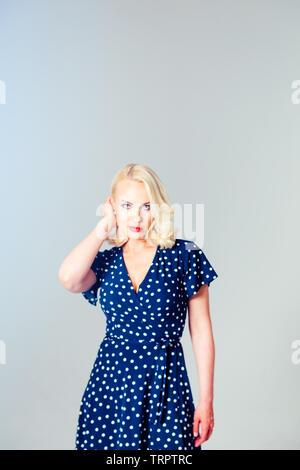 Portrait de studio de belle blonde femme dans une robe bleu foncé blanc contre fond uni Banque D'Images