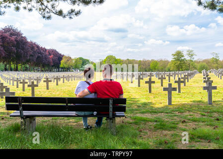 Ysselsteyn, Pays-Bas - le 23 mai 2019. Une paire de jeunes gens assis sur un banc à la croix en béton à au cimetière de guerre allemand. Banque D'Images