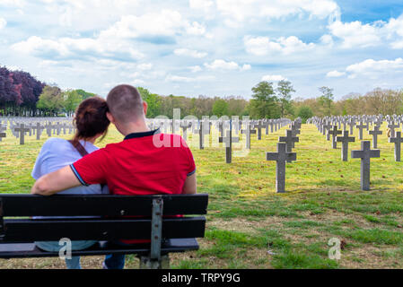 Ysselsteyn, Pays-Bas - le 23 mai 2019. Une paire de jeunes gens assis sur un banc à la croix en béton à au cimetière de guerre allemand. Banque D'Images