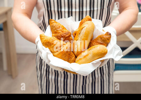 Petits pains et croissants frais dans le panier sur la toile de fond. Baker détient un tablier habillé et savoureuse pâtisseries appétissants pour le petit-déjeuner dans l'hôtel. Banque D'Images