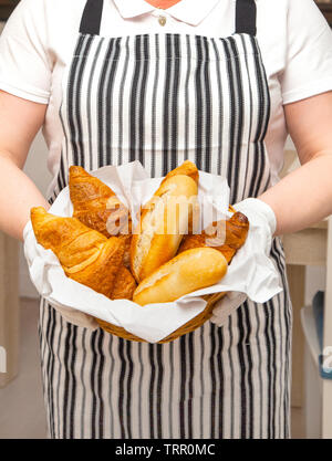 Petits pains et croissants frais dans le panier sur la toile de fond. Baker détient un tablier habillé et savoureuse pâtisseries appétissants pour le petit-déjeuner dans l'hôtel. Banque D'Images