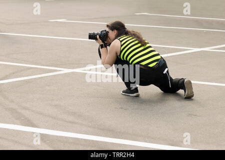 Une femme photographe avec appareil photo reflex numérique est secrètement prendre des photos de quelqu'un dans le parking. Photographier, cachés concept paparazzi Banque D'Images