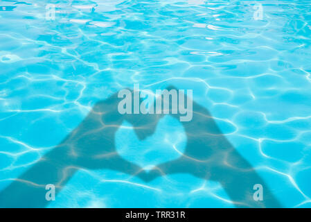 Ombres de mains formant un coeur bleu sur fond de l'eau de piscine d'été, concept Banque D'Images