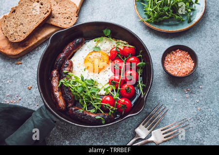 L'heure du petit déjeuner, œuf frit avec saucisses et tomates cerises dans une casserole de fer noir, servi microgreens. Banque D'Images