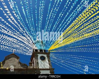 Une place de l'église décorée avec des guirlandes colorées pour une fête traditionnelle à Ténérife. Le bleu-blanc-drapeaux jaunes soufflent dans le vent sous une sombre blu Banque D'Images