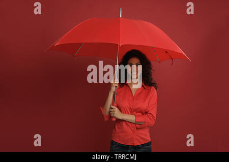 Jeune femme indienne tenant un parapluie rouge et souriant Banque D'Images