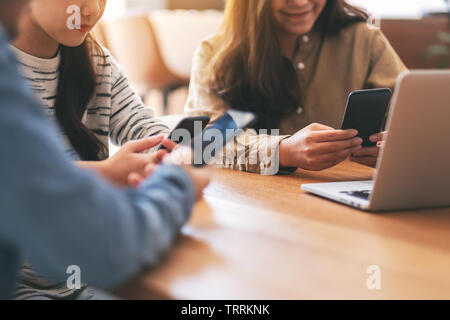 Trois jeunes gens de l'Asie et l'aide à la recherche sur téléphone mobile et ordinateur portable sur une table en bois Banque D'Images