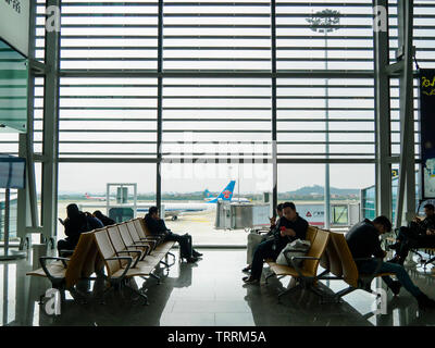 , BAIYUN de Guangzhou, Chine - 10 MAR 2019 - Les passagers de s'asseoir et d'attendre à la porte d'embarquement à l'intérieur de l'Aéroport International de Baiyun. Un avion est visible dans le bac Banque D'Images