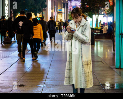 SHANGHAI, CHINE - 12 MAR 2019 -Une jolie jeune femme chinoise sur son smartphone à l'East Nanjing Road (Nanjing Dong Lu) rue piétonne Banque D'Images