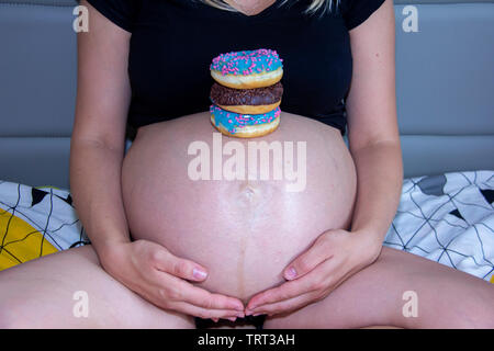 Femme enceinte avec des beignets sucrés sur le ventre. La grossesse et la nutrition. Femme enceinte bénéficiant des beignes. Concept de l'attente et la santé. Banque D'Images