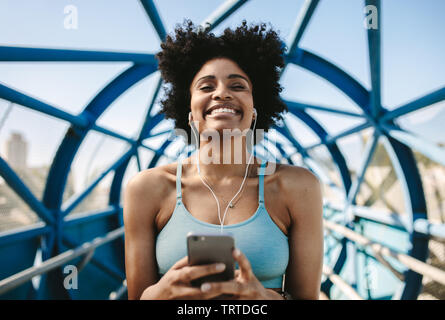 Happy female runner plaisir à l'écouter de la musique depuis son téléphone après run. Femme africaine à se détendre après l'entraînement. Banque D'Images