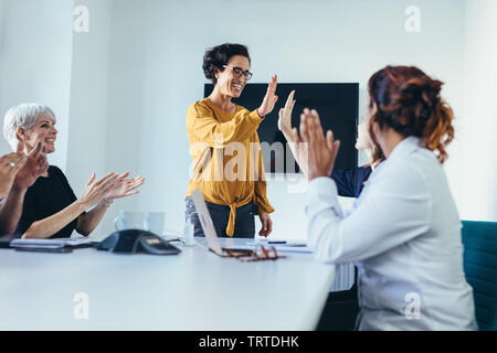 Happy Business team dans les tenues à la table de conférence offrant un rapport cinq ans à l'autre, célébrer la réussite. L'équipe d'entreprise de démarrer un nouveau projet. Banque D'Images