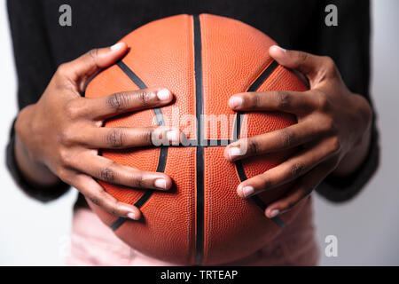 Gros plan de deux femmes à la peau sombre hands holding basket-ball en cuir orange. Isolé sur gray Banque D'Images