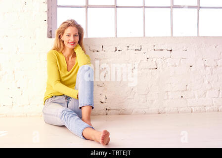 Longueur totale de la grenaille blonde femme d'âge moyen avec un beau sourire de détente sur le plancher. Banque D'Images
