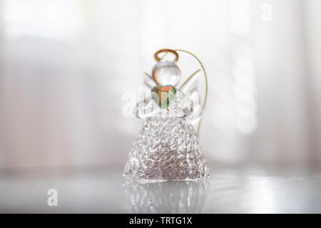 Petit Ange en verre avec un coeur vert dans les mains se dresse sur une table lumineuse au centre. Lumière douce bokeh Banque D'Images