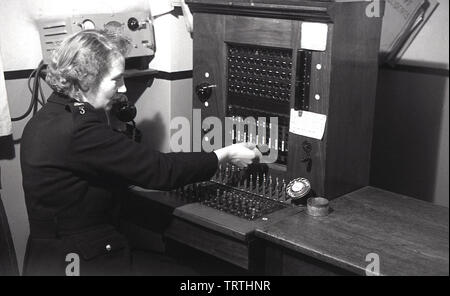 Années 1950, photo historique montrant une femme agent de police en uniforme de l'actionnement manuel d'un standard téléphonique, England, UK. En ce moment des appels ont d'acheminé ou connecté via un central téléphonique centrale par l'utilisation d'opérateurs manuels. Banque D'Images
