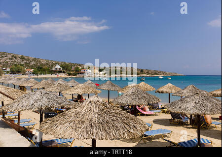 Paille Tropical parasols et chaises longues sur une plage grecque dans une baie de sable avec la mer et le ciel bleu Banque D'Images