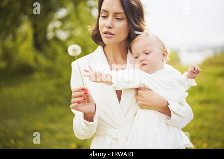 Piscine fashion portrait de jeune belle mère et fille mignon petit souffle de pissenlit sur le pré vert. Image printemps Banque D'Images