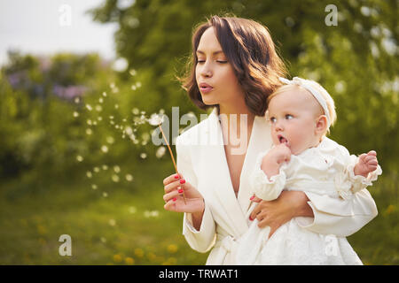 Piscine fashion portrait de jeune belle mère et fille mignon petit souffle de pissenlit sur le pré vert. Image d'été Banque D'Images