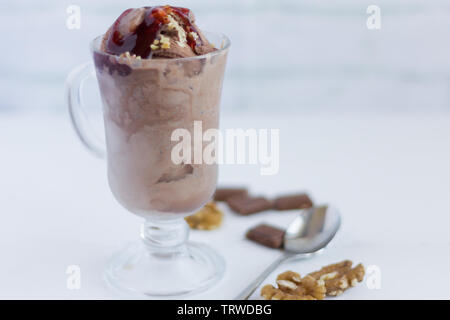 Glace au chocolat aux noix et sauce aux canneberges dans un verre sur un fond clair Banque D'Images